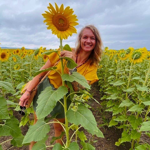 Naomi standing beside a tall sunflower in a bright garden setting